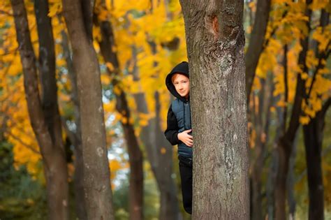 Premium Photo Boy Hiding Behind Autumn Trees In The Park