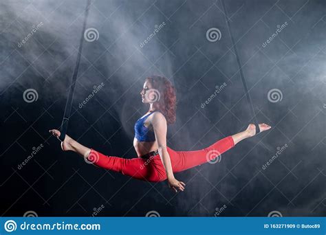 female athletic and flexible aerial circus artist with redhead on aerial straps on black
