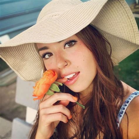 a woman wearing a hat and holding a flower in her mouth while sitting on a bench