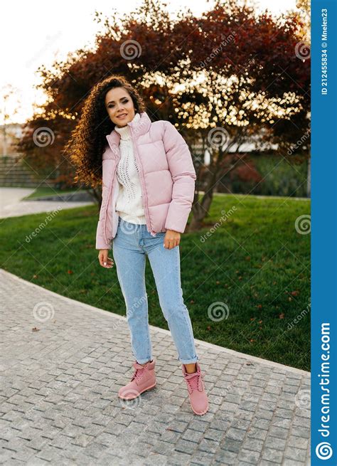 On The Walkway In The Park Stands A Beautiful Girl In A Pink Light