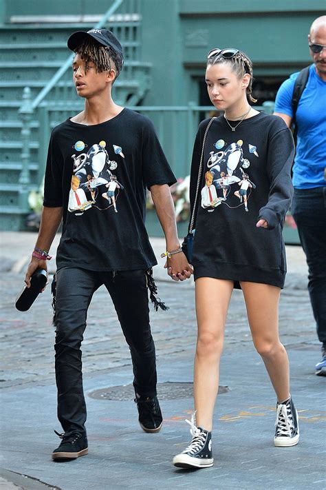 A Man And Woman Are Walking Down The Street Holding Hands With Each Other While Wearing Matching