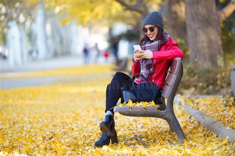 Beautiful Young Woman Sitting In A Bench And Using Her Mobile Phone In