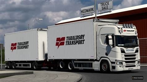 A White Semi Truck Driving Past A Red And White Building With A Sign On