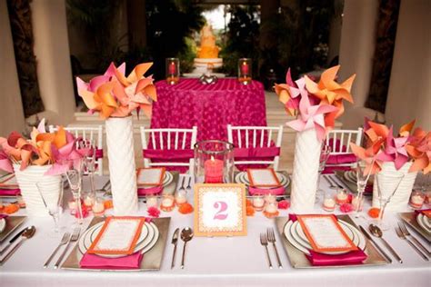 The Table Is Set With Pink And Orange Napkins Silverware And White Vases