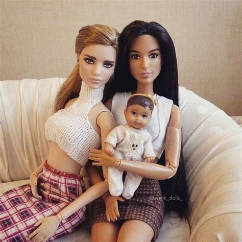Two Barbie Dolls Sitting Next To Each Other On A Couch With One Holding A Doll