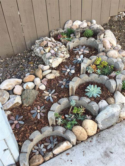 A Rock Garden With Succulents And Rocks In The Middle Along Side A Fence