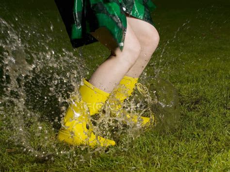Woman Wearing Rubber Boots Jumping In Rain Puddle People Outdoors