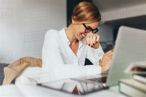 Business Woman In Spectacles Sitting At Her Desk In Office And Laughing