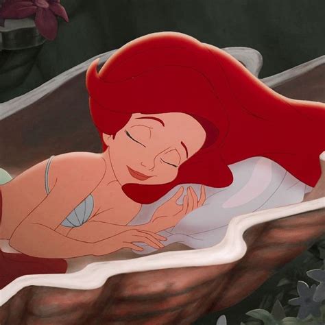 the little mermaid is laying down and hugging her face with another person in the background