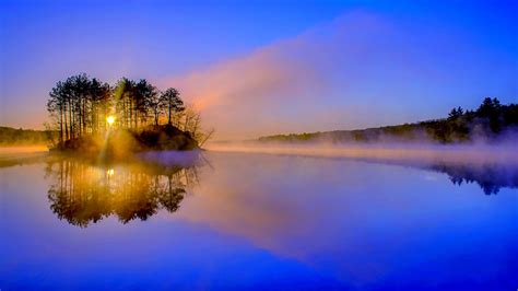 Landscape View Of Trees Under Blue Sky Fog Covered River During Sunset