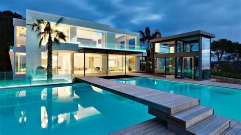 A House With A Swimming Pool In Front Of It At Night Surrounded By