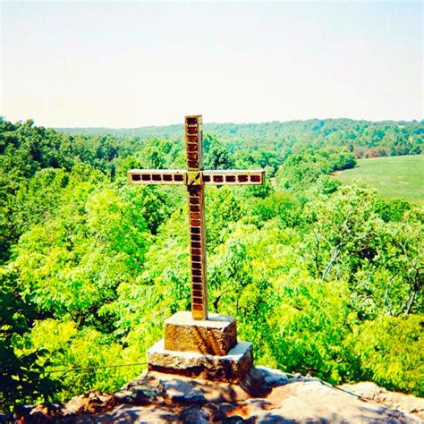 A Wooden Cross Sitting On Top Of A Rock In The Middle Of A Lush Green Forest