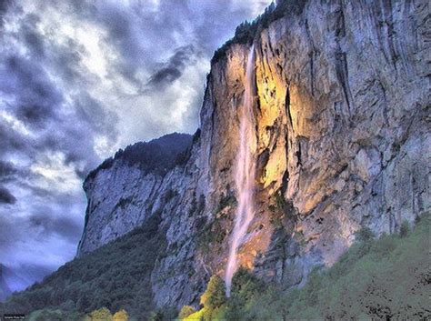 A Large Waterfall Cascading From The Side Of A Mountain Under Cloudy