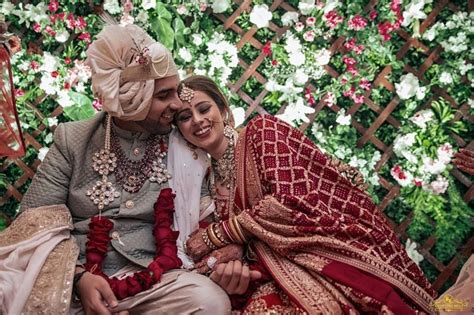 A Man And Woman Sitting Next To Each Other In Front Of A Flower Covered Wall