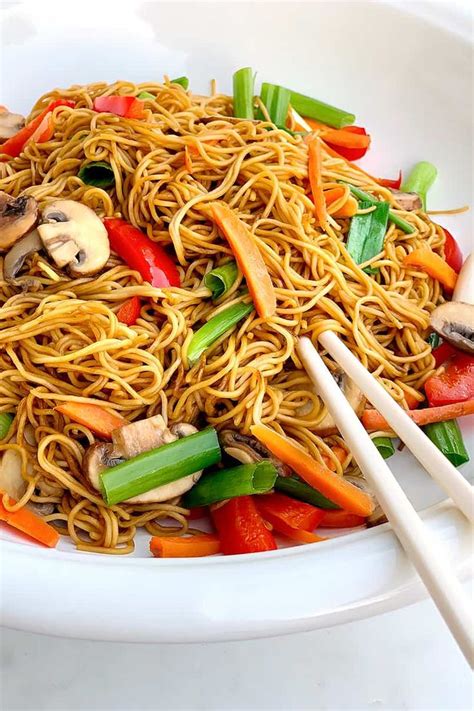 A White Plate Topped With Noodles And Veggies Next To Chopsticks On A Table