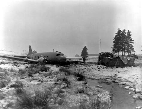 US Army soldier standing next to a C-47 Skytrain wreck, near Bastogne