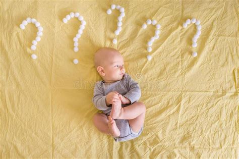 Top View Of Infant Child Lying Surrounded With Question Marks Made Of