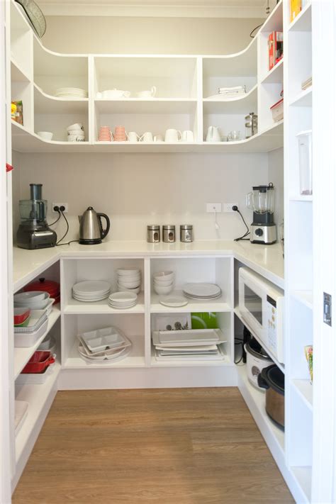 A Kitchen With White Cabinets And Shelves Filled With Plates Bowls