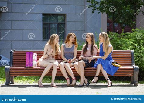 Group Of Four Young Women Sitting On Bench In Summer Park Stock Image