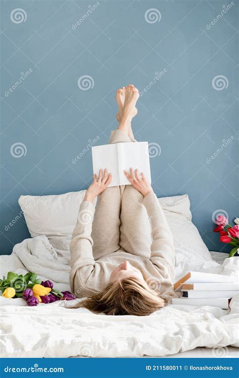 Happy Woman Lying On The Bed Wearing Pajamas Reading A Book Stock Image