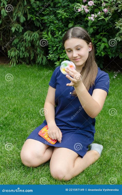 A Teenage Girl Is Playing With A Spinner Anti Stress Toy Outside On The Lawn Smiling Stock