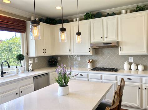 A Kitchen With White Cabinets And Lights Hanging From The Ceiling Over