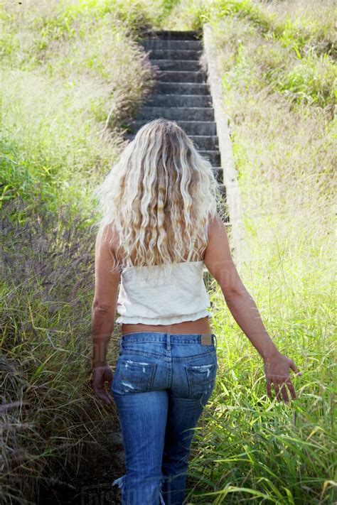 A Young Woman With Long Blond Hair Walks Through The Tall Grass Towards