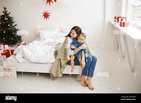 Happy Mother Covered With A Blanket And Her Daughter Sitting On The Edge Of The Bed In A Bright