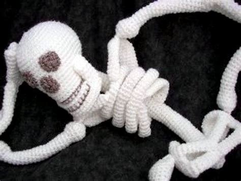 A Crocheted Skeleton Laying On Top Of A Black Surface With Its Head