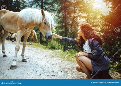 Young Woman With Curly Hair Petting A Horse In The Woods Stock Photo