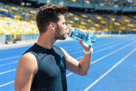 Attractive Young Man Drinking Water After Training At Sports Stadium