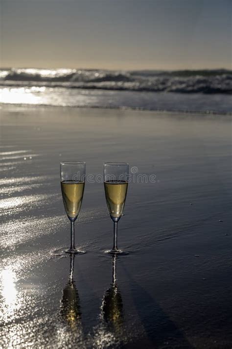glasses of cava or champagne sparkling wine on white sandy ocean beach with water waves on