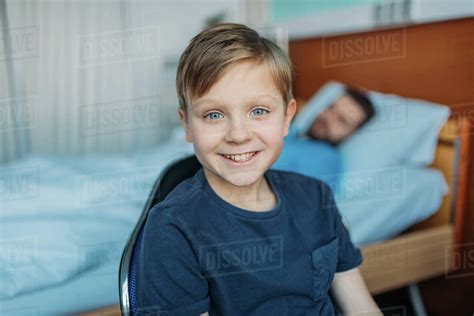 Little Son Sitting On Chair Near His Sick Father Sleeping On Hospital Bed At Ward Dad And Son