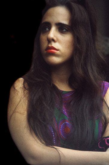 A Woman With Long Dark Hair Wearing A Colorful Dress And Holding Her