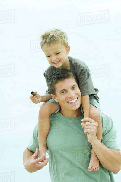 Father Carrying Son On Shoulders Smiling At Camera Stock Photo