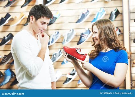 Female Sale Assistant Demonstrates Shoe To Man At Footwear Shop Stock