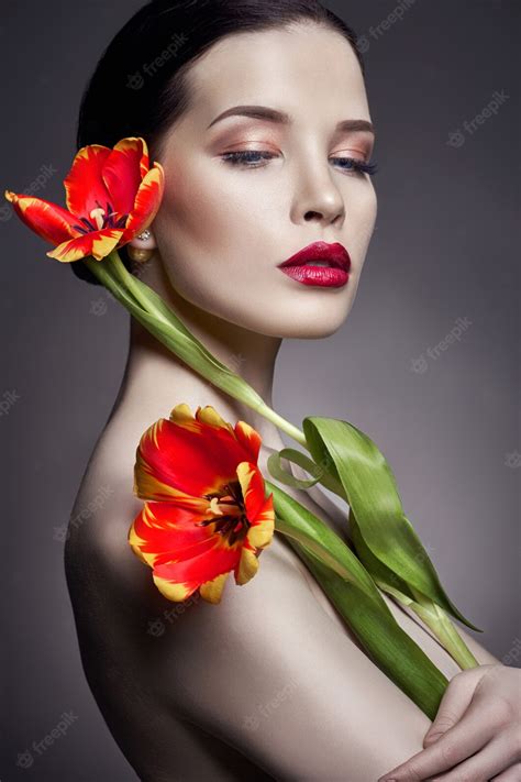 手にチューリップの花と完璧な肌、セクシーな裸のブルネットの女性と裸の裸の女の子。夏の顔と手のスキンケア。明るいナチュラルメイク プレミアム写真