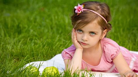 Cute Little Girl Is Holding Face With One Hand Lying Down On Grass