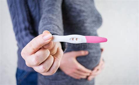 Young Pregnant Woman And Her Husband Holding Swollen Belly With Pregnancy Test In Her Hand Stock
