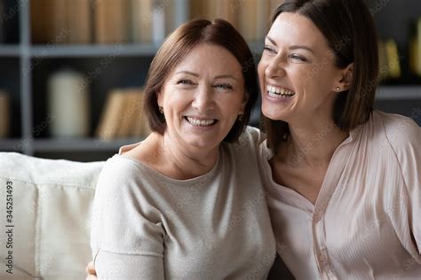 Happy Mature Mother And Adult Daughter Hugging Close Up Having Fun Sitting On Couch At Home