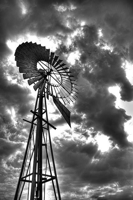 A Black And White Photo Of A Windmill With Clouds In The Sky Behind It