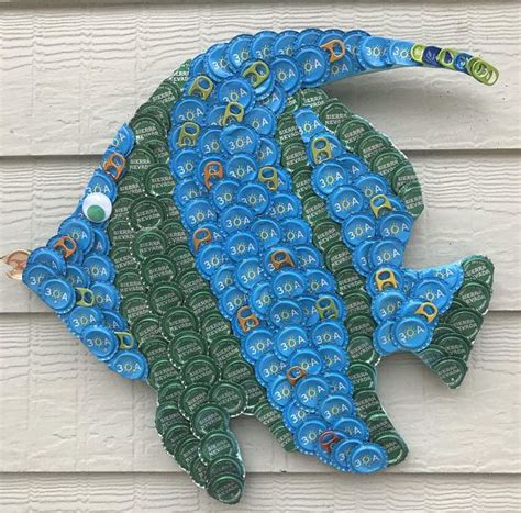 A Blue And Green Fish Made Out Of Plastic Bottle Caps On A White House Wall