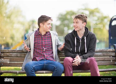 Two Young Male Friends Chatting On Park Bench Stock Photo Alamy