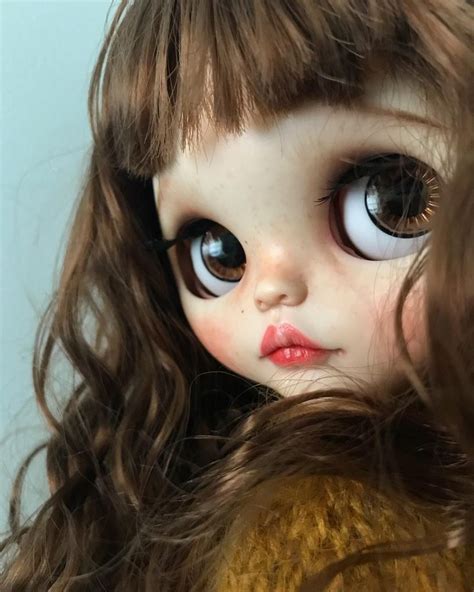 A Close Up Of A Doll With Big Blue Eyes And Long Brown Hair Wearing A