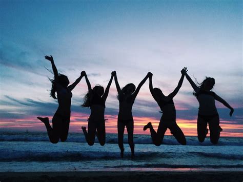 four women jumping in the air at sunset on the beach with their arms raised up