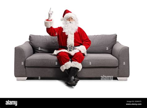 Santa Claus Sitting On A Gray Sofa And Pointing Up Isolated On White