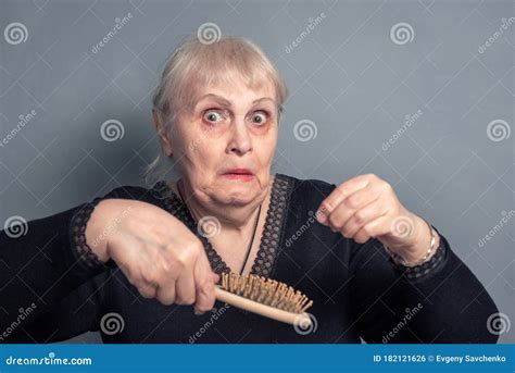 en äldre kvinna med kamb i handen och en överraskad bild av grå bakgrund arkivfoto bild av