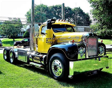 A Large Yellow Semi Truck Parked On Top Of A Lush Green Field Next To Trees