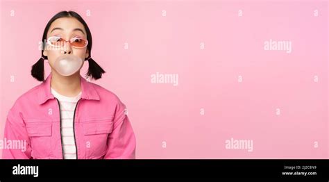 stylish asian girl blowing bubblegum bubble chewing gum wearing sunglasses posing against
