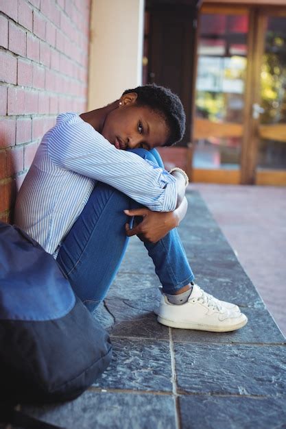 Premium Photo Portrait Of Sad Schoolgirl Sitting Against Brick Wall